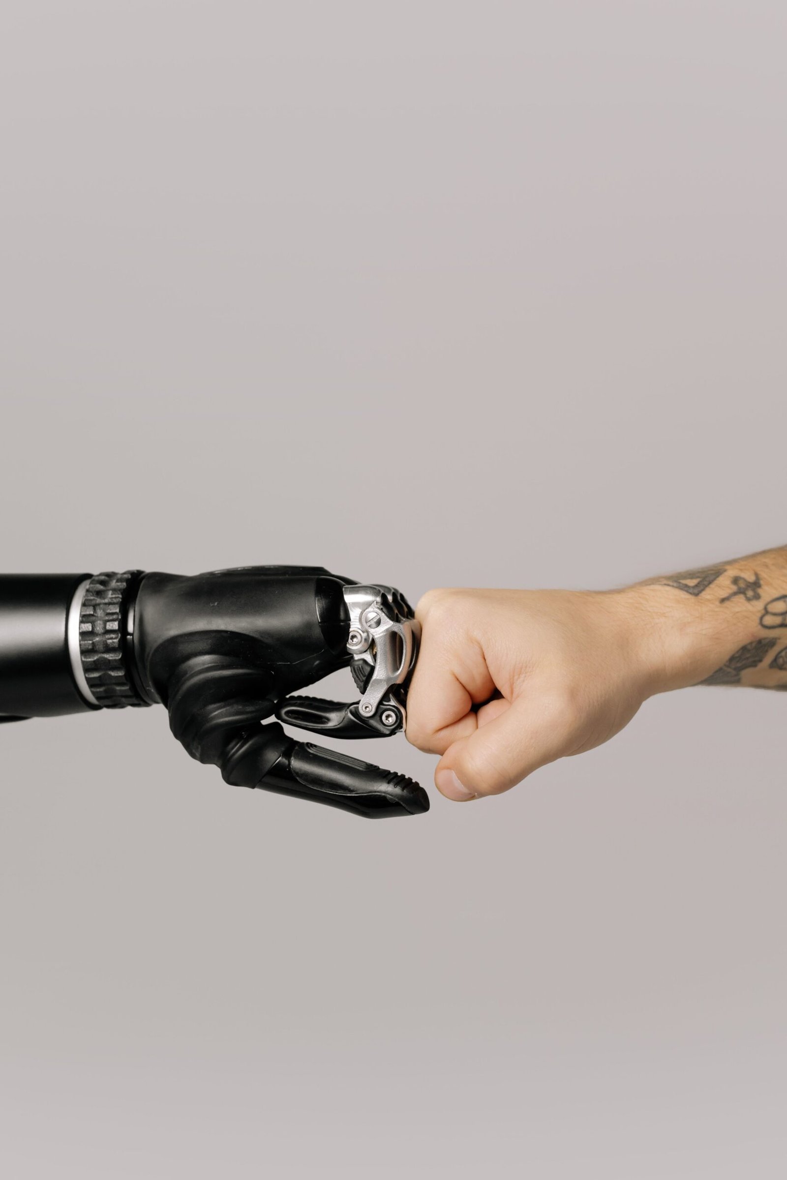 Close-up of a human fist bumping a robotic prosthetic hand, symbolizing handing a goal over to a machine and trusting it to run