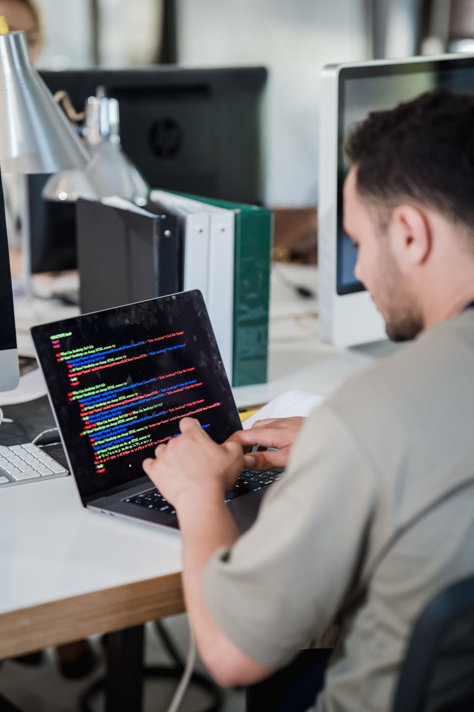 A young software developer typing code on a laptop in a modern office